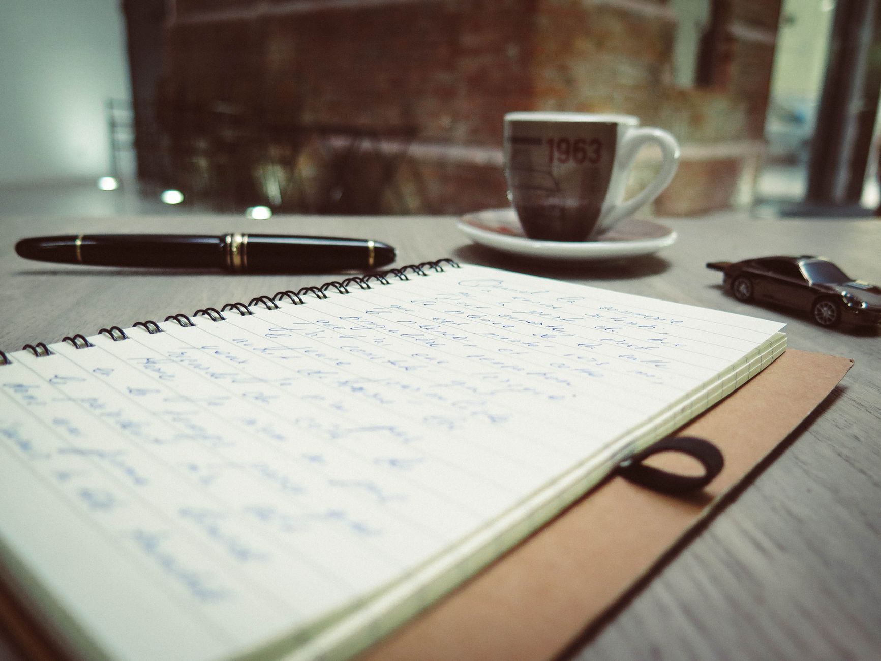 Notesbog, fyldepen og kaffekop på et bord